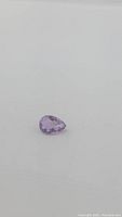 Photo of a single pear-shaped natural purple amethyst gemstone on a white background, showing the stone's size, shape, and clarity.