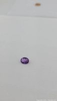 Front angle view of the natural oval cut purple amethyst gemstone on a white surface showing color and facets