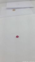 Oval cut natural ruby gemstone on a white surface, showing size and color