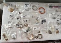 Multiple small bags containing bracelets, rings, earrings, and brooches on a white background.