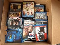 Box open showing multiple DVD and Blu-ray cases with visible titles including Avatar, Olympus Has Fallen, God Grave of the Wings, Wild Hogs, The Day the Earth Stood Still, Law Abiding Citizen, Swing Vote.