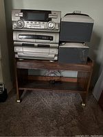 Full shot of Emerson stereo system components placed on wooden cart with speakers on top and floor, showing overall configuration and condition