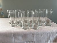Front view of 13 clear glasses: 6 large and 7 smaller, arranged in two rows on a white cloth surface.