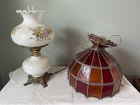 Table lamp with white glass and floral design next to Tiffany style stained glass hanging lamp showing color and design