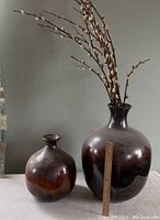 Two large brown ceramic vases on a beige cloth background, one with a ruler showing about 14 inches tall with decorative branches inside