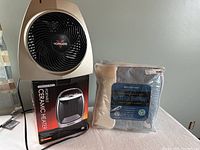 Vornado fan, Wexford portable ceramic heater box, and two new beige heated throws in packaging.