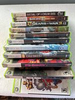 Stack of ten Xbox 360 game cases showing spines and partial front covers, various genres visible with wear to covers.