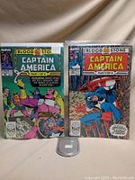 Two Captain America comics, Bloodstone Parts 1 and 2, front covers visible and displayed upright on a gray stand.