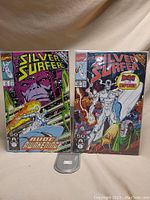 Two Silver Surfer comic books issue 51 and 53 displayed upright showing front covers, with vibrant comic art and protected in bags.