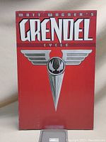 Front cover of 'Matt Wagner's Grendel Cycle' graphic novel book showing red background with white title and silver emblem.