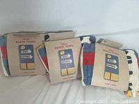 Three Disney branded beach towels in original packaging showing colorful signpost design with 'Beach' and 'Happiness'.