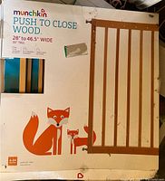 Image showing Munchkin Push To Close Wood Safety Gate box with gate partially visible, measurements 28 to 46.5 inches wide, 30 inches tall, fox art on box.