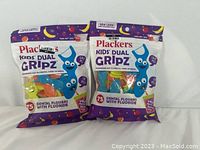 Two sealed packs of Plackers Kids Dual Gripz Dental Flossers in colorful packaging, featuring cartoon characters and product info.