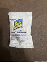 Front view of a single SoftScrub Sparkle Automatic Dish Detergent pack showing phosphate-free label, quantity (1 oz), brand name, and caution warnings.
