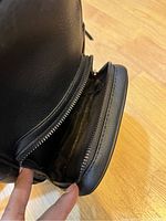 Close-up of smaller front zippered pocket interior showing black fabric lining and wear.