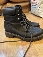 Side view of boots showing black leather, thick sole, lace-up front, and padded collar.