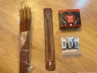 Incense sticks, wooden incense holder, small box of backflow incense cones, and three bottles of essential oils on wooden surface