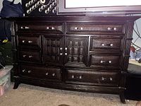 Front view of dark wood 8-drawer dresser with detailed panel doors in center and marble top, showing wood texture and metal handles.