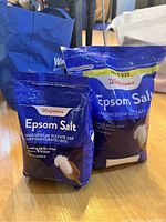 Two blue Walgreens Epsom Salt bags of different sizes on a hardwood floor with other bags in the background