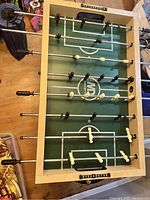 Foosball table showing the full playing surface, player figures on rods, and green field markings.