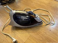 Front side view of a used black and white Black+Decker steam iron with chrome accents, power cord visible lying on floor.