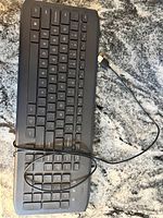 Black wired USB keyboard with complete key layout on a granite countertop.