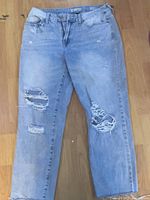 Light blue denim jeans with multiple horizontal rips, fraying and distressing visible on front side.