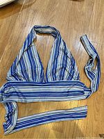 Blue and white striped halter neck tank top laid flat on wooden floor.