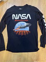 Black long sleeve shirt with NASA space explorer graphic on the front and print on sleeve