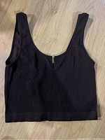 Black ribbed cropped tank top with front zipper is shown laid flat on wood floor.