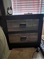 Front view of the 2 drawer nightstand against wall near window, showing drawer handles and wood texture.
