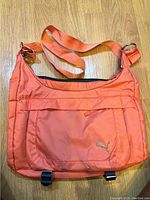 Front view of pink Puma shoulder bag showing exterior with front zippered pocket and logo