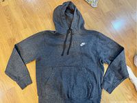 Gray Nike hooded sweatshirt laid flat on wood floor, showing front, hood, and drawstrings.