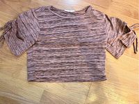 Pinkish short-sleeve knit top with crew neck and tie sleeves laid flat on wooden floor