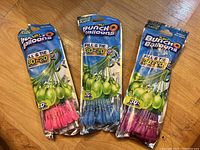 Three unopened packs of Bunch o Balloons water balloons in various colors pink, blue, and pink again shown in packaging on wooden surface