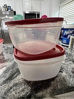Two large Tupperware containers stacked with red lids visible, sitting on a countertop.