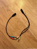 Black 3.5mm audio splitter cable with two female ports and one male plug on wooden surface.