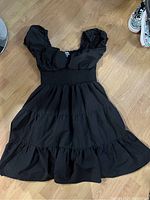 Short black dress with puff sleeves and ruched waist detail lying on wooden floor