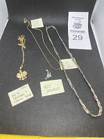 Overview of four jewelry items on black mat: 14K gold necklace with eagle charm, goldtone chain, silver rope chain, and sterling M pendant