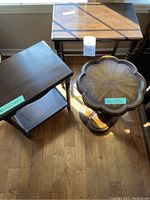 Three wooden occasional tables with distinct shapes and sizes placed on wood floor, showing surface wear and sunlight reflections.