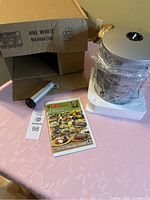 Photo showing the marinator device wrapped in plastic, the pump, the open box marked 'Nine Minute Marinator', and the manual on the table.