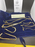 Photo showing six pieces of gold-toned jewelry including two necklaces and four bracelets displayed on a blue velvet holder with label indicating measurements.