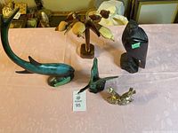 Photo of assorted bird and fish figurines on table, showing Blue Mountain Pottery fish (green-blue glazed), wooden bird carvings, and a dark carved wooden bird sculpture.