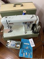Full view of Brother sewing machine set up on table with accessories, manual, and green carrying case