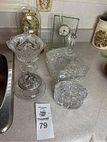 Photo showing four crystal covered dishes with ornate cut-glass designs along with two clocks placed behind them on a kitchen counter.