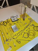Full overview of assortment of jewelry displayed on yellow cloth, includes necklaces, bracelets, earrings in silver and gold tones, some pieces on jewelry stand