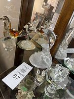 View of multiple glass and crystal figurines including swan, dolphin, rabbit, duck, and other animals displayed on mirrored shelves.