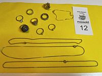 Photo showing all rings arranged with necklaces and a bracelet on a yellow cloth.