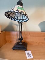 Adjustable table lamp with stained glass shade shown turned off, displaying geometric and colored pattern on shade, black base with switch.
