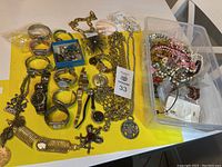Overview of assorted jewelry including watches, bracelets, necklaces, and a plastic bin of loose earrings and small items.